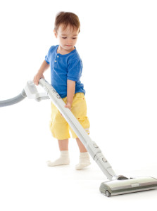 Toddler is cleaning room with vacuum cleaner isolated on white